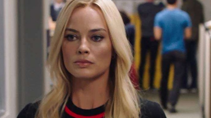 Margot Robbie in a black top walking along an office