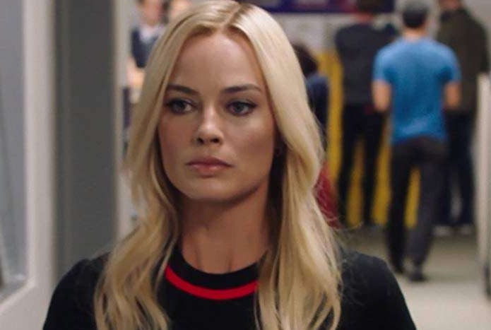 Margot Robbie in a black top walking along an office