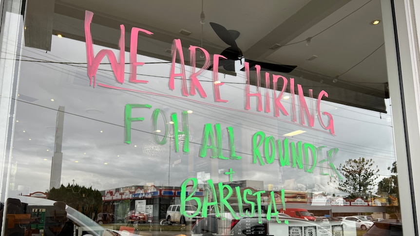 A paint pen sign on a window reads: WE ARE HIRING FRONT OF HOUSE ALL ROUNDER AND BARISTA!