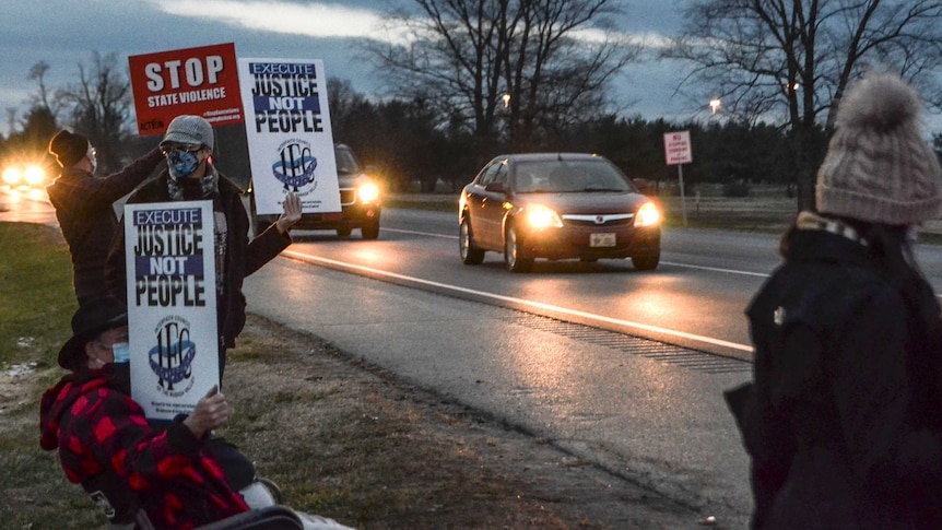 Demonstrators stand along a road holding placards protesting against the death penalty