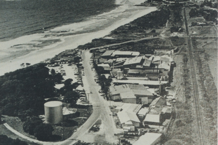 An aerial black and white photo of series of sheds and buildings right behind the sand at the beach