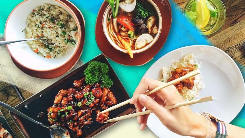 Bowls of tom yum soup, fried rice and marinated meat, with a hand using chopsticks to eat the Thai food.