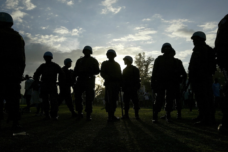 A group of UN peacekeepers in a field, all in silhouette 