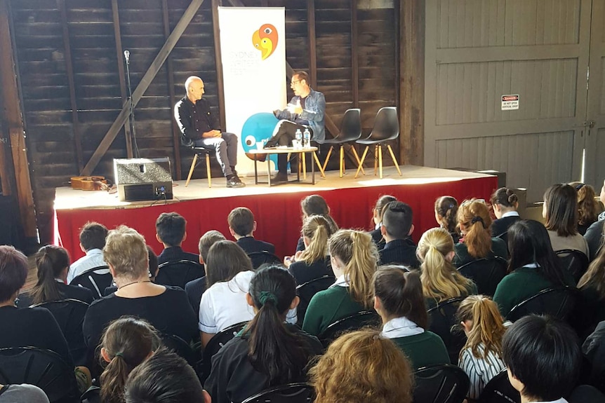 Peter Evans and Paul Kelly on stage having a conversation in front of an audience of school students.