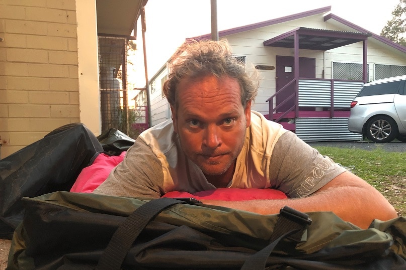 A man in a sleeping bag outside a public toilet block