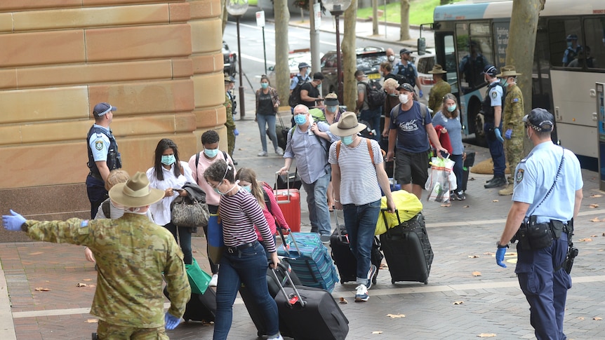 people wearing masks and pulling bags with wheels walk on the footpath