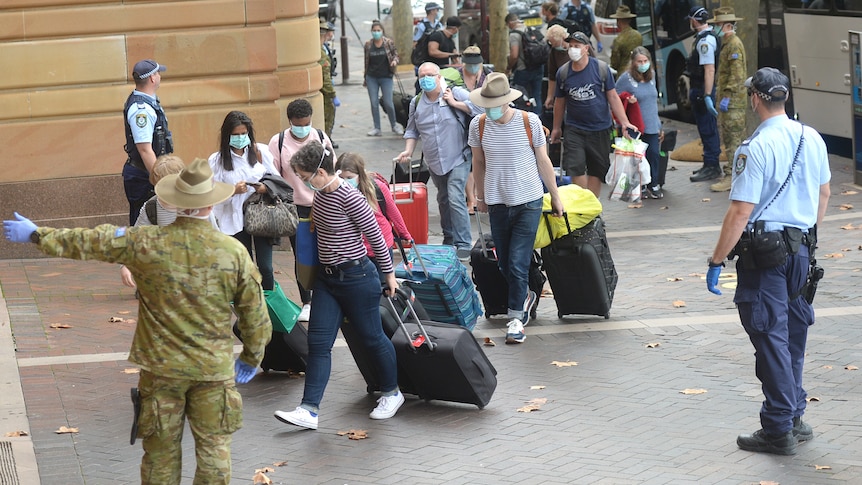 An army officer directs people from a bus into hotel quarantine.