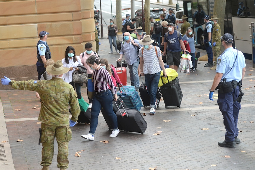 An army officer directs people from a bus into hotel quarantine.