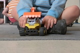 Child in blue and grey striped jumper playing with a toy truck