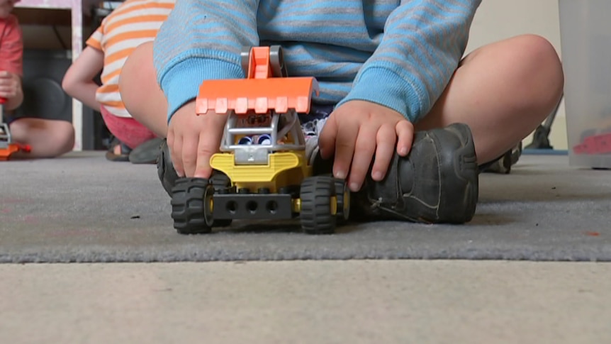 Child in blue and grey striped jumper playing with a toy truck