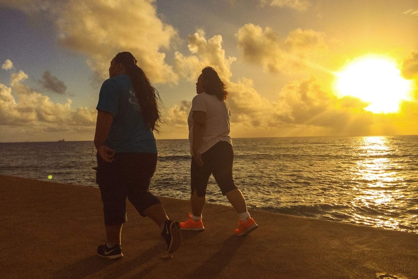Two women walk on a beach at sunset.