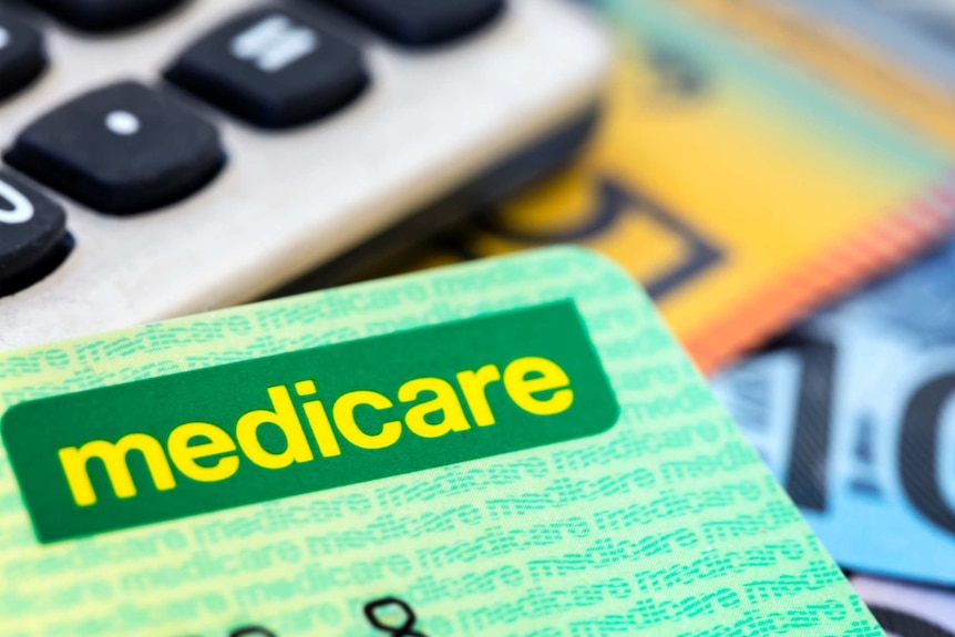 Close-up of a green Medicare card with a calculator and money in the background