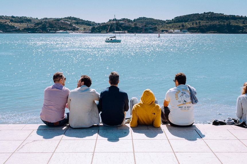 group of male friends sitting by the water