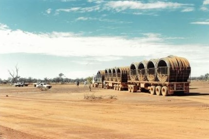 A truck with a large trailer load of black piping parked in a bare paddock