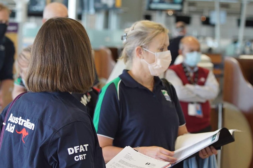 A woman in a face mask next to a woman in a blue shirt with 'Australian Aid' written on the back