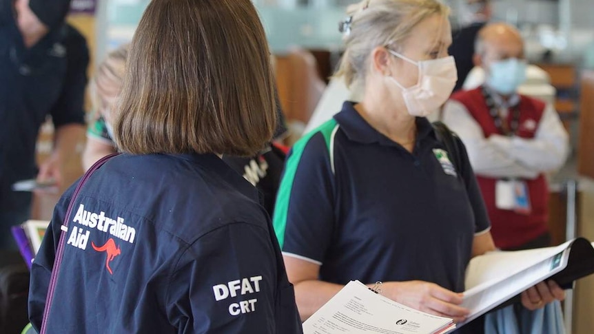 Women in an airport wearing a mask, and another with the Australian Aid logo on her back.