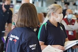 Women in an airport wearing a mask, and another with the Australian Aid logo on her back.