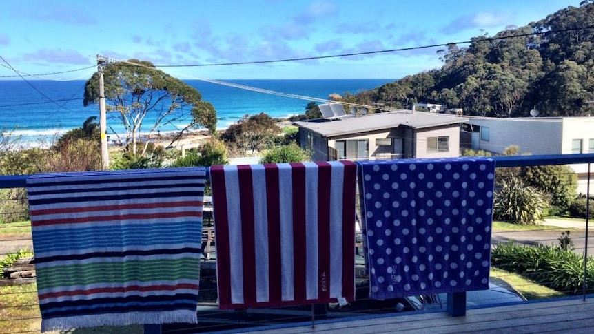 Towels hang over a balcony railing, with the beach behind.