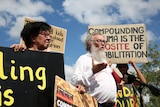 An Indigenous woman and a white man holding placards and talking to the media.