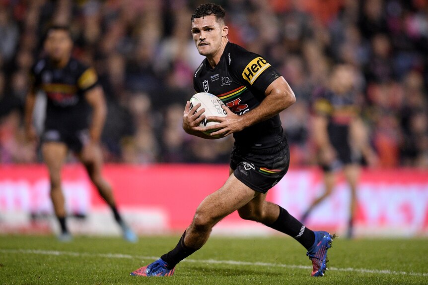 A Penrith Panthers NRL player holds the ball in two hands during a night match.