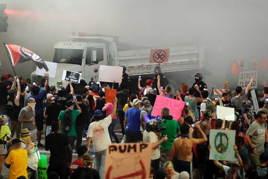 Protesters rally in the foreground as police deploy pepper spray