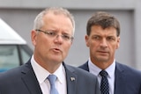 PM Scott Morrison speaks to media in Canberra as Angus Taylor, frowning, watches on.