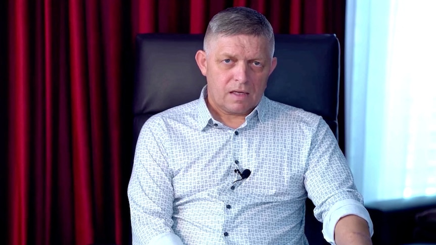Robert Fico sits in a leather chair and speaks to the camera looking serious, wearing a patterned button-up shirt