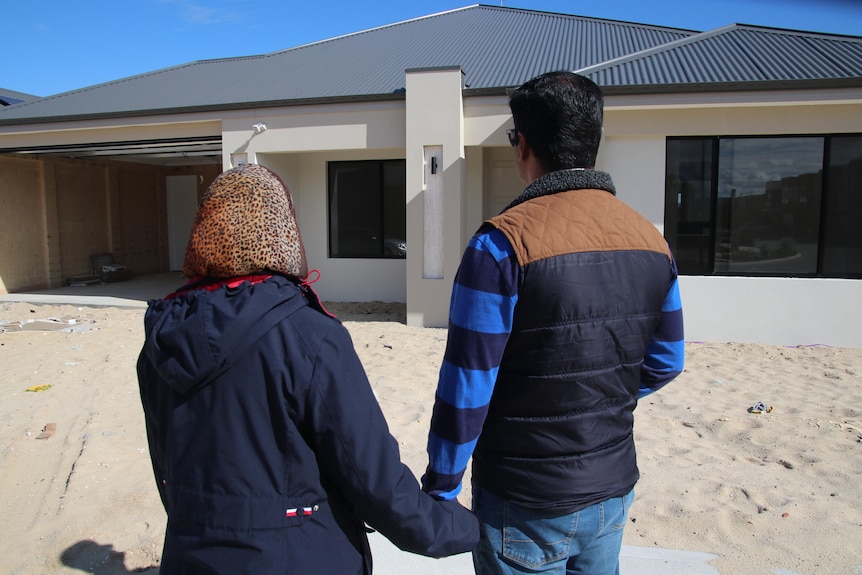 Una vista trasera de una pareja cogidos de la mano mirando su casa recién construida. 