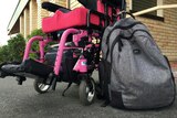 A backpack sits next to a pink, electric wheelchair.