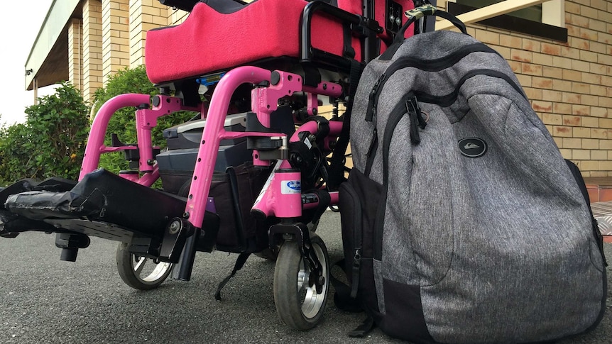 A backpack sits next to a pink, electric wheelchair.