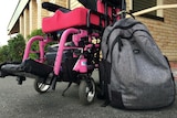 A backpack sits next to a pink, electric wheelchair.