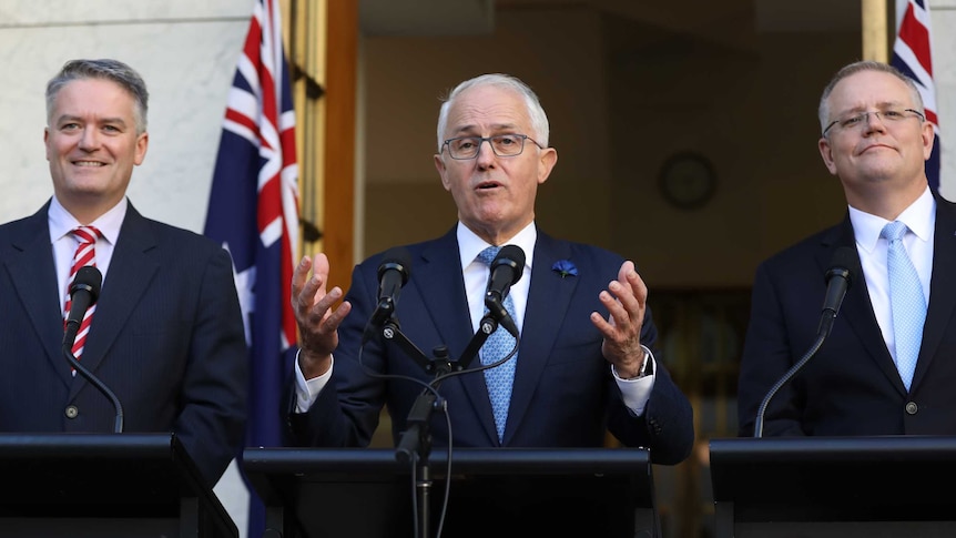 Malcolm Turnbull grips a lecternMathias Cormann is smiling widely on the PM's right, Scott Morrison has a tight-lipped grin.