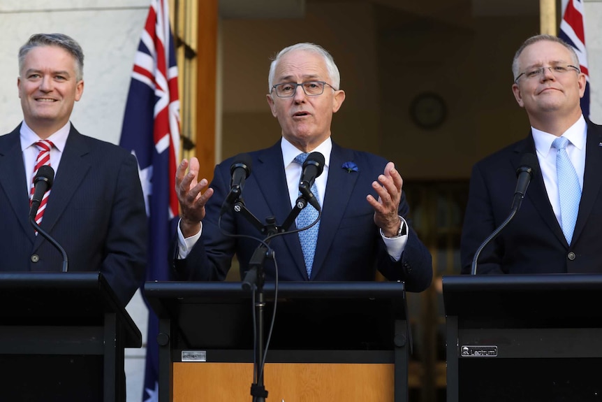 Malcolm Turnbull grips a lecternMathias Cormann is smiling widely on the PM's right, Scott Morrison has a tight-lipped grin.