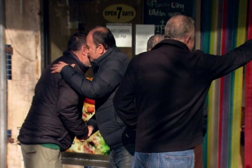 Two men greet and embrace each other in a street.