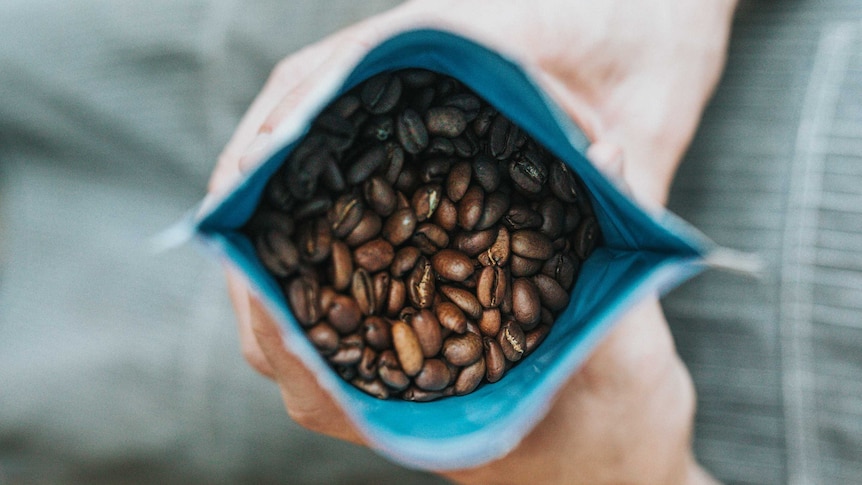 A person holds an opened bag of coffee beans.