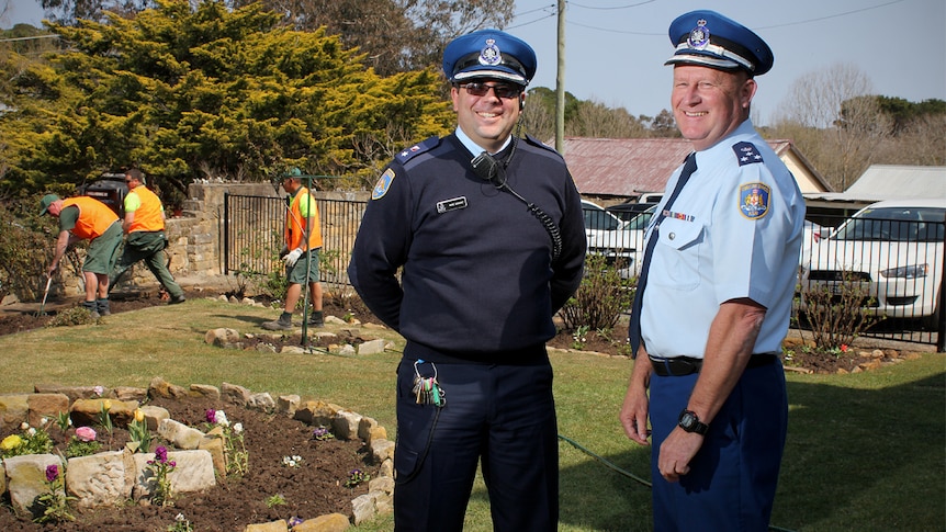 Mark Derwent and Mick Reid face the camera at Berrima jail's gardens while inmates work behind them.