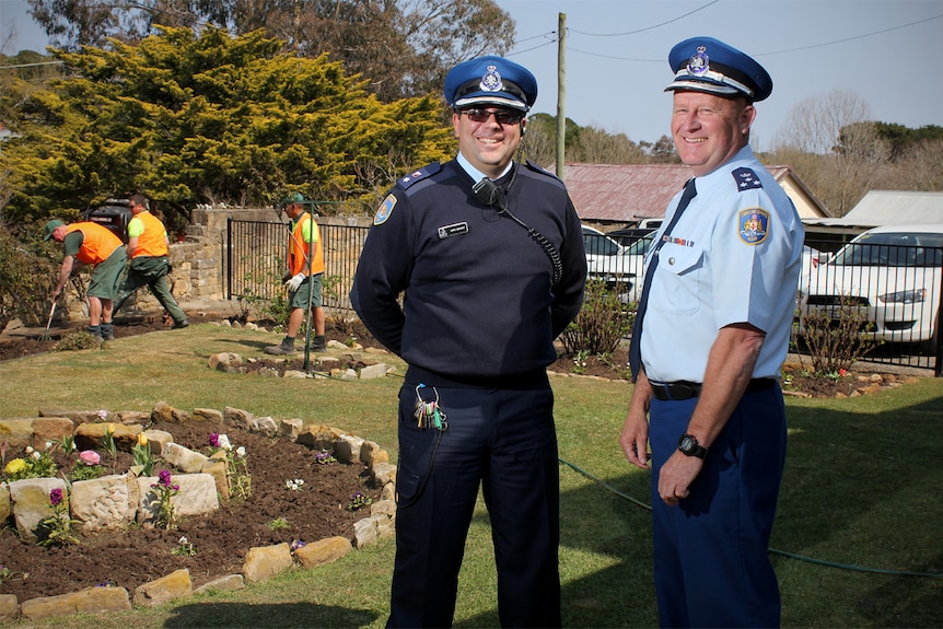 Mark Derwent and Mick Reid face the camera at Berrima jail's gardens while inmates work behind them.