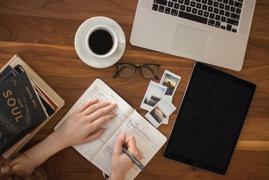 Bird's eye view of someone sitting at a wooden table while writing in a journal.