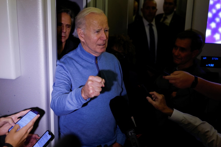 Image of Joe Biden sticking his fist up while wearing a blue zip up jumper on an airplane.