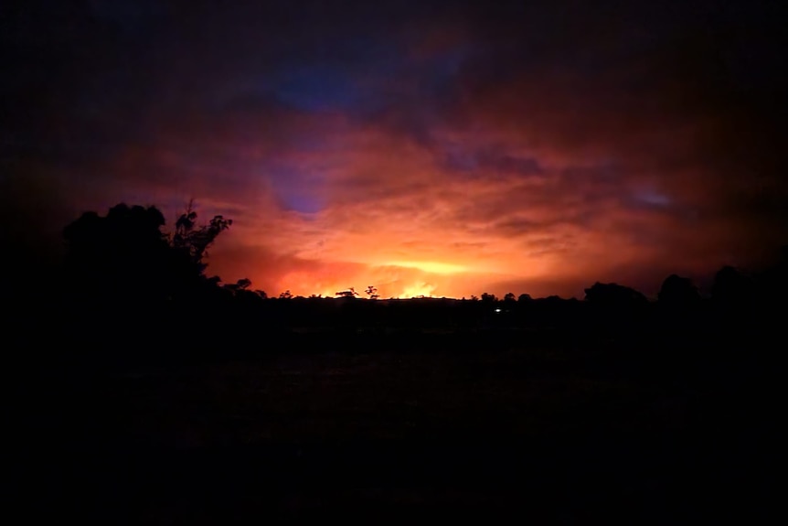 Long-distance image of a fire burning at night in bushland.