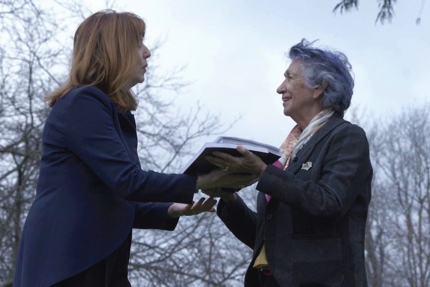 Yoorrook Justice Commission chair Eleanor Bourke handing a document to a woman representing the Victorian government. 