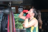 A woman with gloves hits a punching ball in a backyard gym