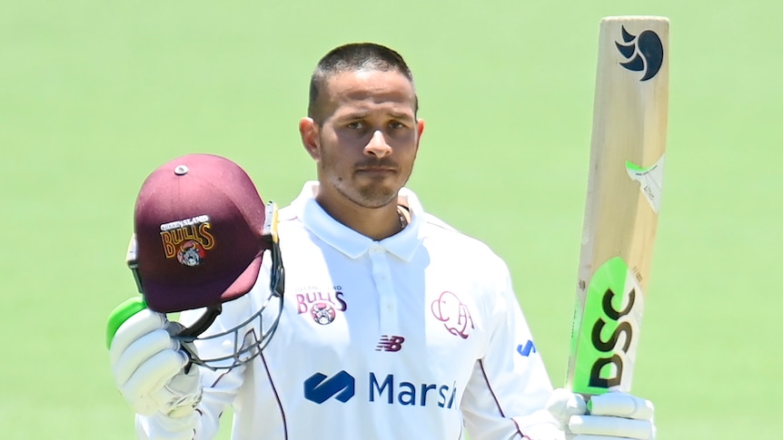 A Queensland Sheffield Shield player raises his bat with his left hand as he celebrates a century.