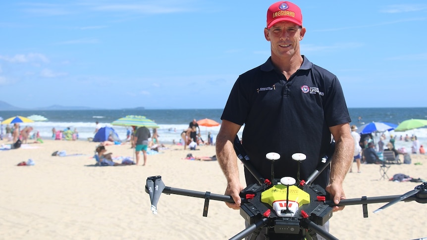 Man standing on the beach holding a drone smiling at the camera.