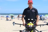 Man standing on the beach holding a drone smiling at the camera.