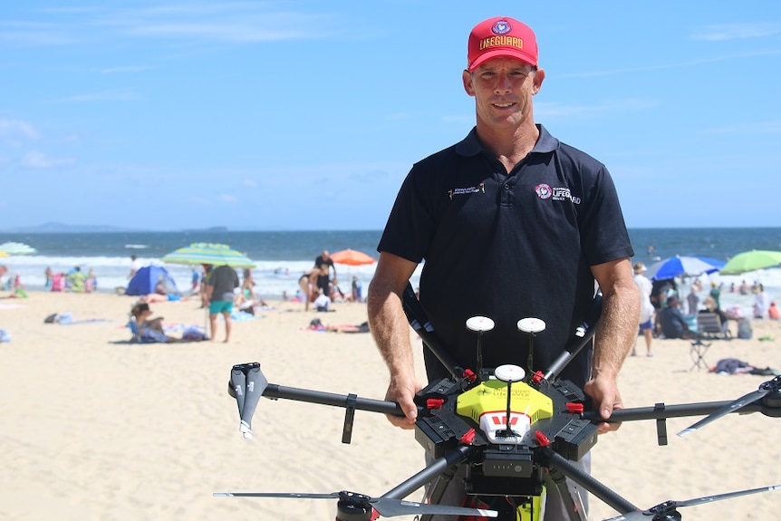 Man standing on the beach holding a drone smiling at the camera.