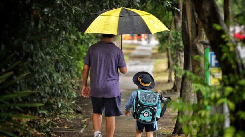A man is holding an umbrella for a school boy.