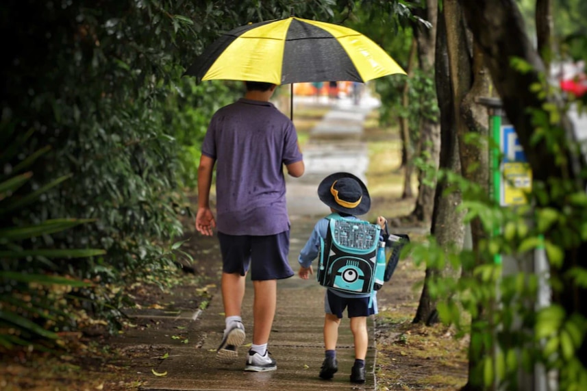 A man is holding an umbrella for a school boy.