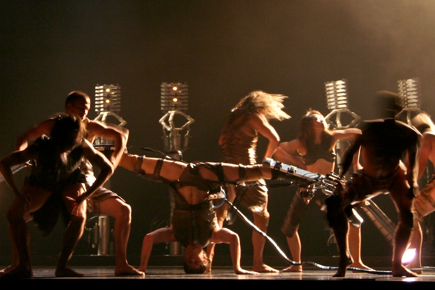 Dancers with prosthetic and mechanical attachments on a stage.
