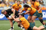 A number of Wallaroos players hang off Luka Connor as she barges through